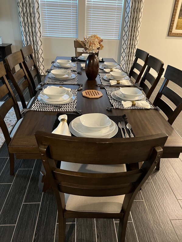 A dining table set with white plates, bowls, and cutlery, surrounded by dark wooden chairs with cushioned seats. - in Glendale Near stadium, entertainment & shopping (Glendale)