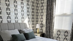 A neatly made bed with a grey blanket and pillows, a bedside table with a lamp, and a patterned wall. - in Glendale Near stadium, entertainment & shopping (Glendale)