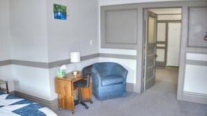 Ein Hotelzimmer mit einem Bett, einem Schreibtisch mit Stuhl, einer Lampe, einem kleinen Schrank und einer Tür zu einem weiteren Raum.