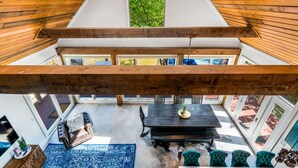 A loft-style room with a high ceiling, exposed wooden beams, a central skylight, a dining area with a table and chairs, and a view of the outdoors. - Elegant Birdhouse Cabin with 🔥Heated🔥 Cowboy Pool (Kyle)