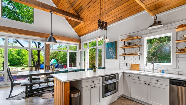 A modern kitchen with white cabinets, a large island, and a view of the outdoors. - Elegant Birdhouse Cabin with 🔥Heated🔥 Cowboy Pool (Kyle)