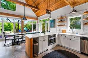 A modern kitchen with white cabinets, a large island, and a view of the outdoors. - Elegant Birdhouse Cabin with 🔥Heated🔥 Cowboy Pool (Kyle)