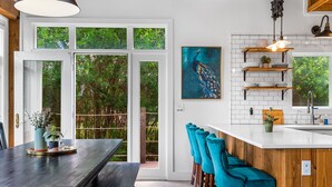 A modern kitchen with white subway tiles, wooden shelves, and a peacock painting. - Elegant Birdhouse Cabin with 🔥Heated🔥 Cowboy Pool (Kyle)