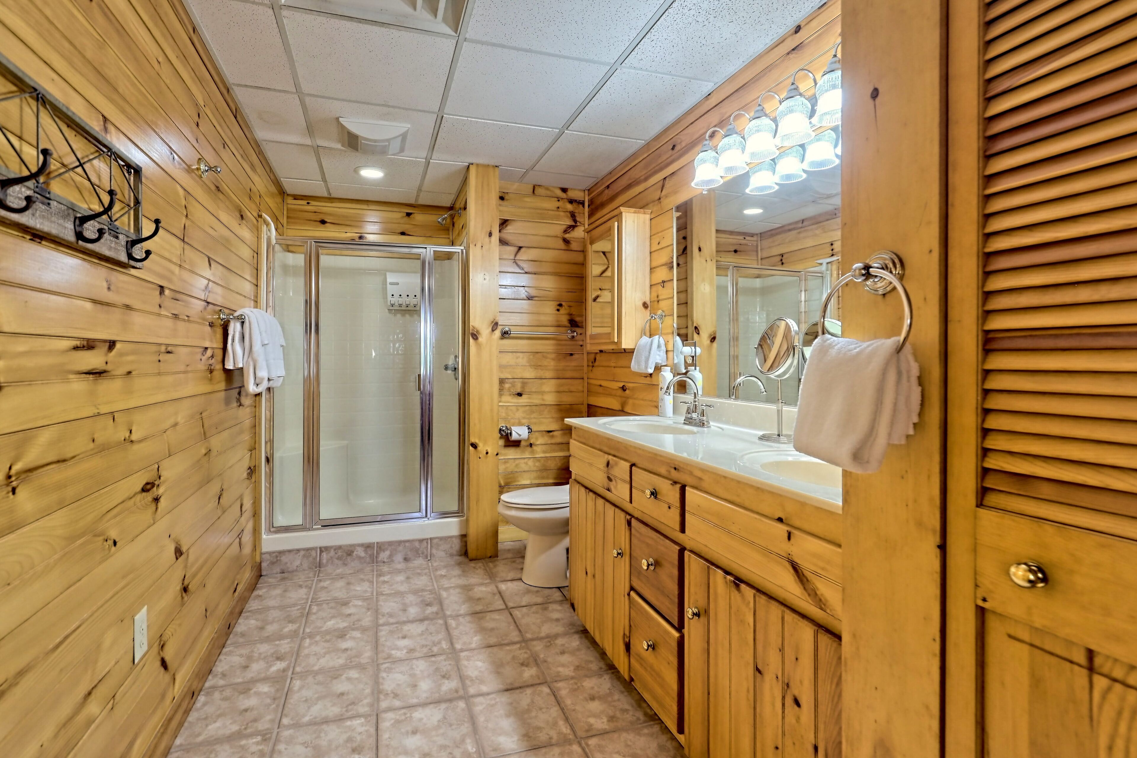 A wooden-paneled bathroom with a shower, toilet, and vanity with a mirror and sink.