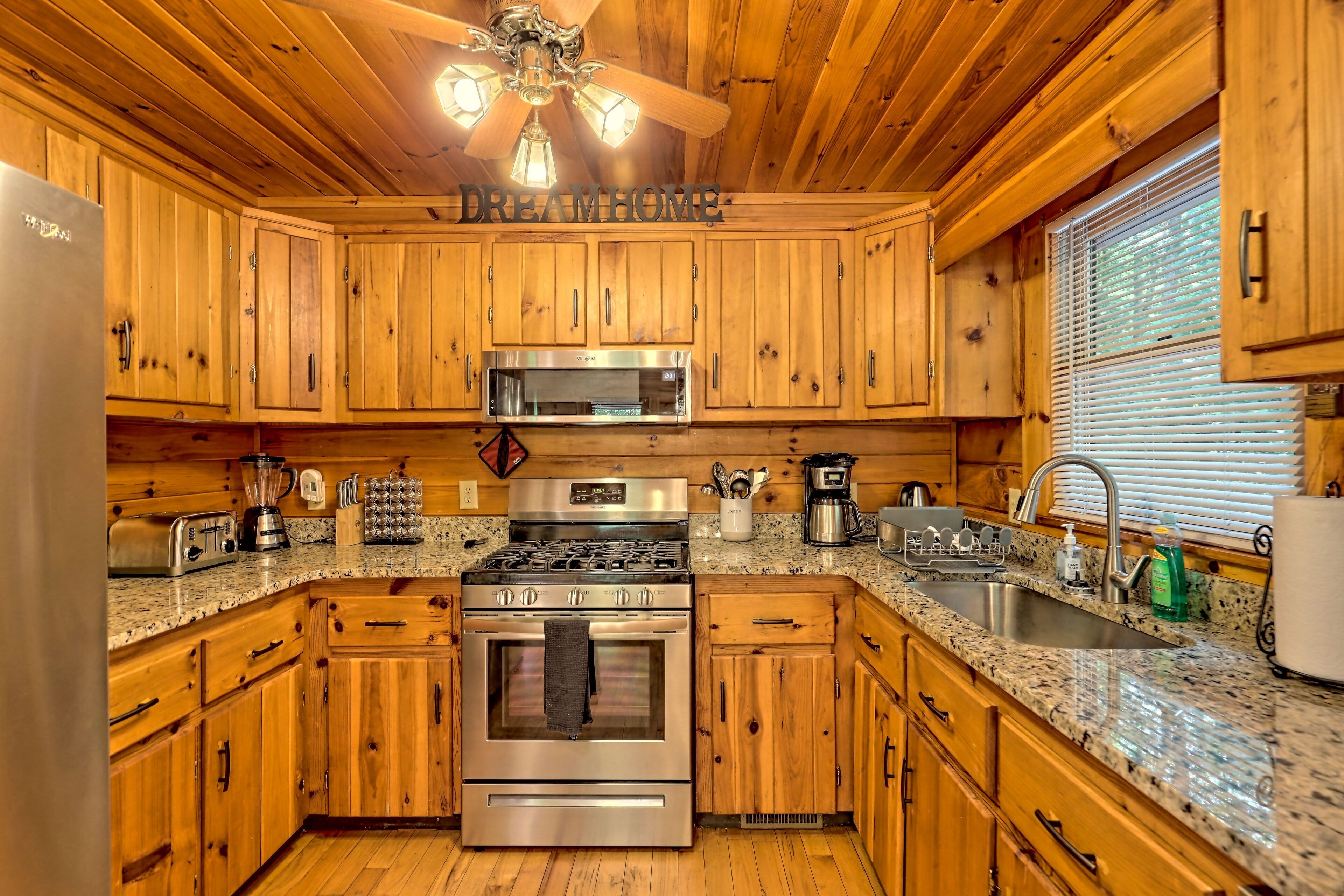 A kitchen with wooden cabinets, stainless steel appliances, granite countertops, and a ceiling fan.