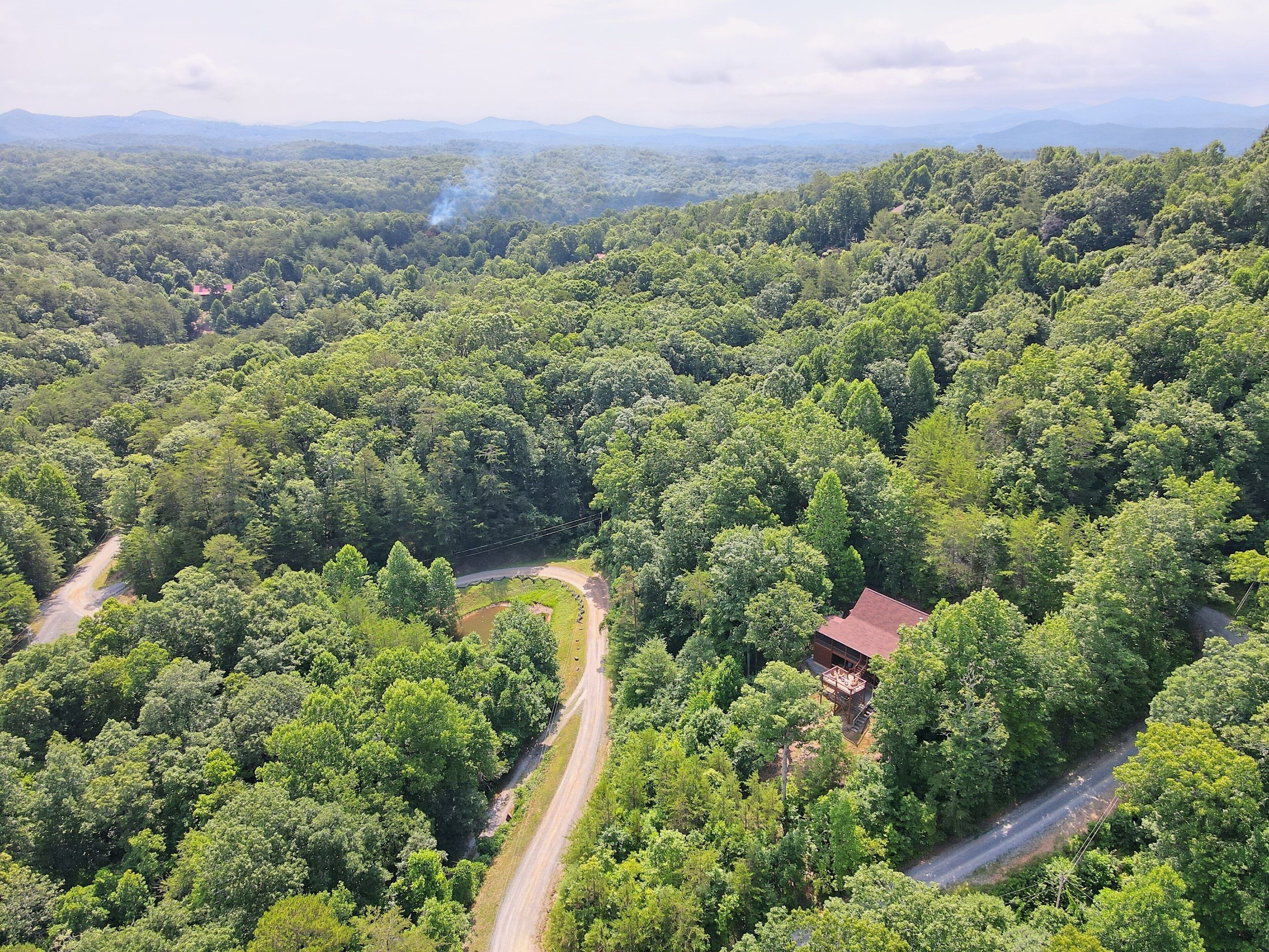 An aerial view of a forested area with winding roads and a building with a red roof.