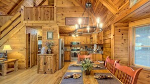 A wooden cabin interior with a dining area, kitchen, and a 'welcome' sign. - Large Deck, Screened Porch, Hot Tub, Fire Pit (Morganton)