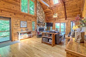 A spacious wooden cabin with a stone fireplace, comfortable seating, and large windows offering views of the surrounding forest.