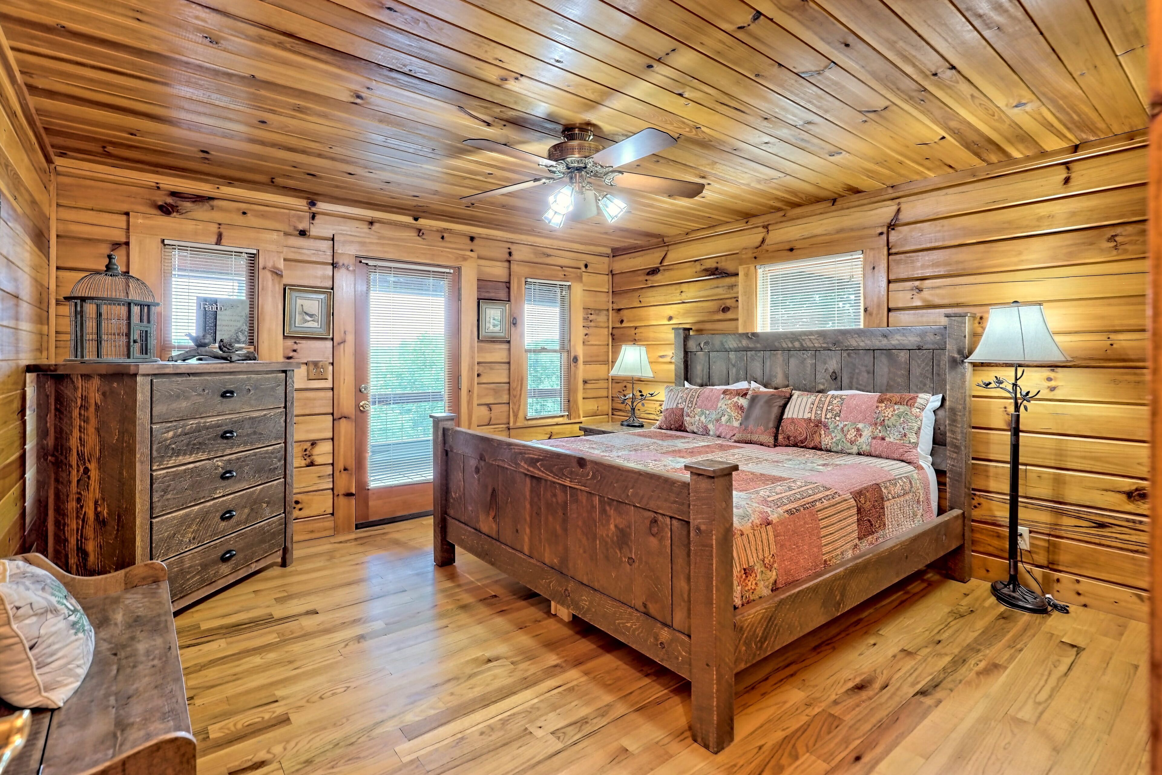 A wooden cabin bedroom with a bed, dresser, and ceiling fan.
