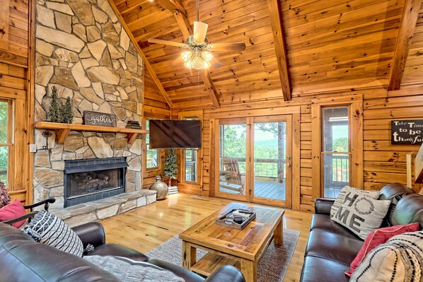 A cozy cabin interior with a stone fireplace, wooden ceiling, leather sofas, and a flat-screen TV.