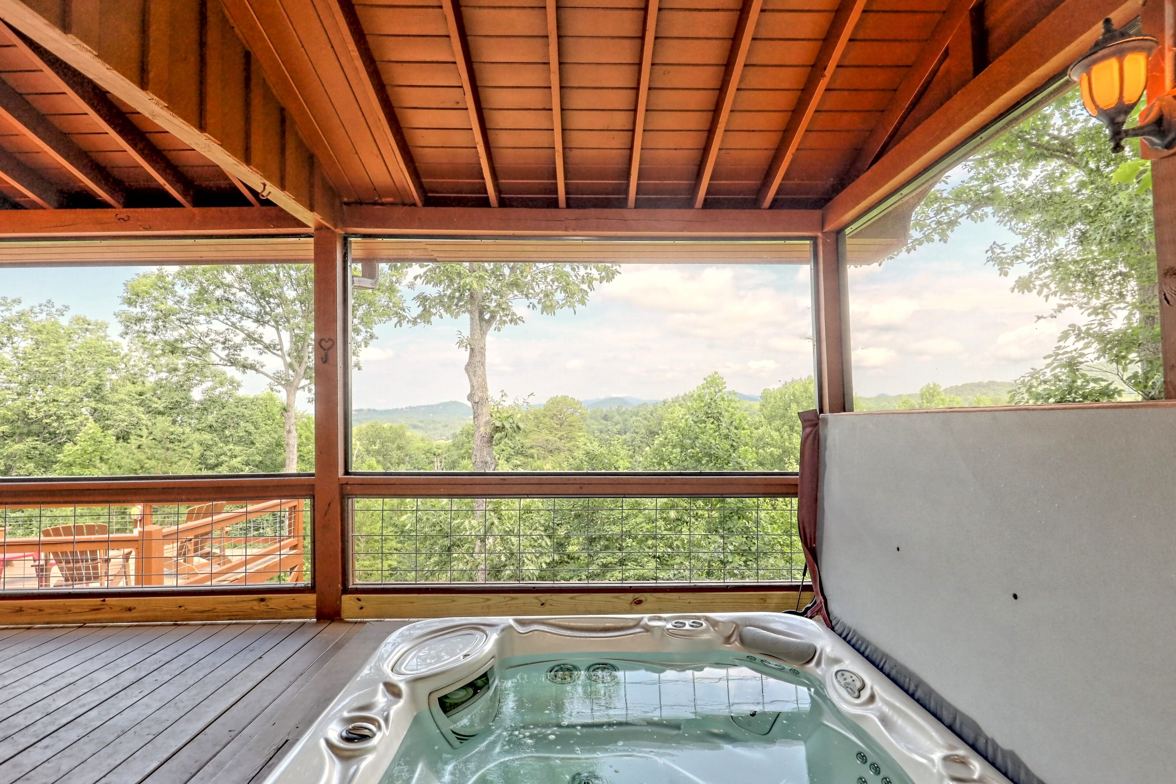 Una vasca idromassaggio su un pontile di legno con vista su una foresta e montagne.