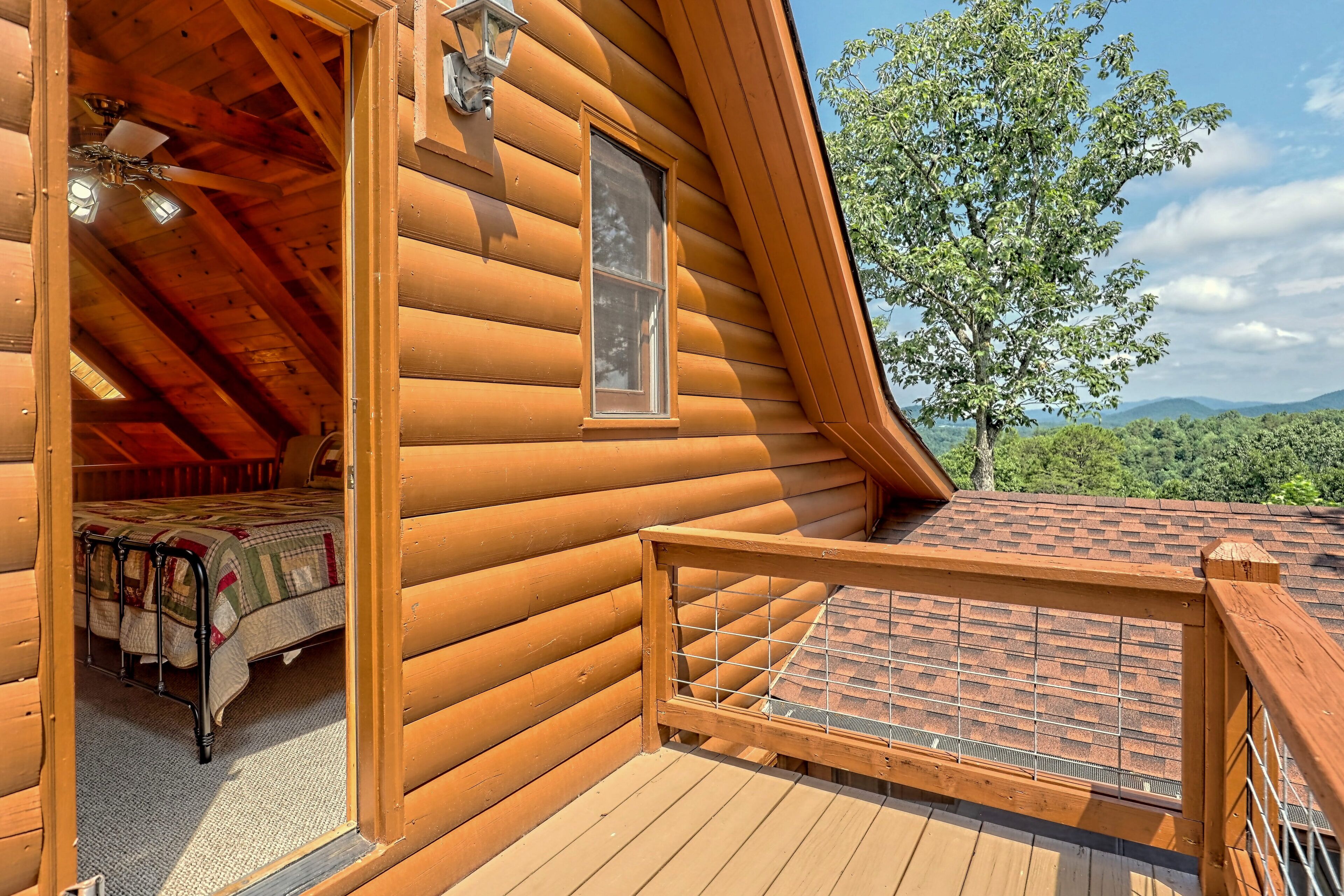 Una cabaña de troncos con un dormitorio en el altillo, una terraza de madera y vistas al bosque circundante.