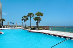 A swimming pool with a clear blue water, surrounded by palm trees and a view of the ocean.