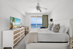 A bedroom with a bed, a dresser, a television, a ceiling fan, and a view of the ocean through a large window. - ENDLESS GULF VIEWS WITH WRAPAROUND BALCONY! (Panama City Beach)