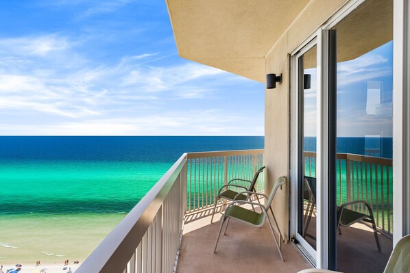 A balcony with a view of the ocean, two chairs, and a glass door. - ENDLESS GULF VIEWS WITH WRAPAROUND BALCONY! (Panama City Beach)