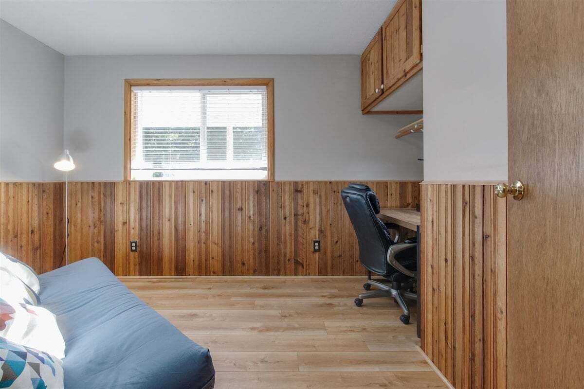 Una habitación con paredes de paneles de madera, una ventana con persianas, un escritorio con una silla y un sofá.