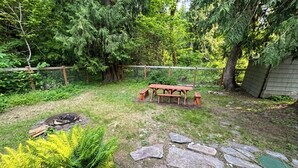 Un patio trasero con un banco de madera, una fogata y un sendero de piedra.