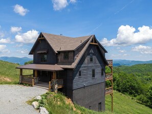 Une maison en bois à deux étages, dotée d’un porche, d’un balcon et offrant une vue panoramique sur les montagnes.