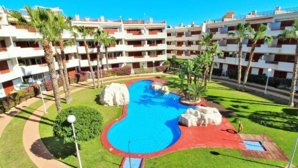 Een resort met een centraal gelegen zwembad, meerdere balkons en palmbomen.