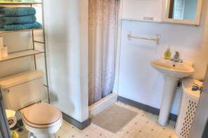 A bathroom with a toilet, sink, shower curtain, and a shelf with towels.