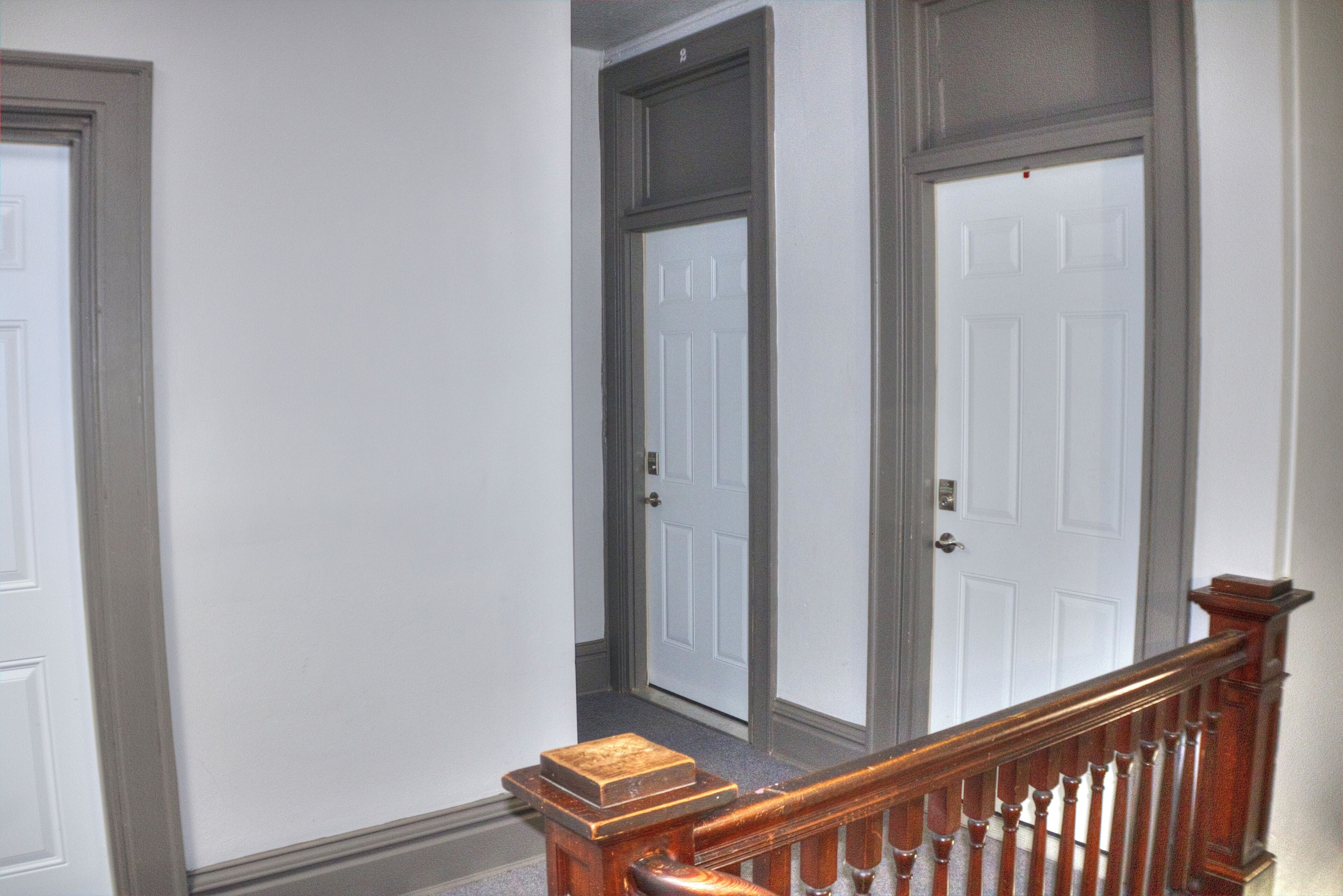 A hallway with two white doors, a wooden handrail, and a carpeted floor.