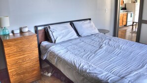 A neatly made bed with a headboard, a wooden dresser, and a lamp on the left side.