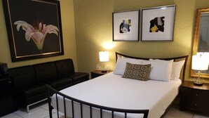 A hotel room with a bed, a black sofa, a nightstand with a lamp, and two framed artworks on the wall. - Wynwood Miami Tropical Hideaway Guest Suite (Miami)