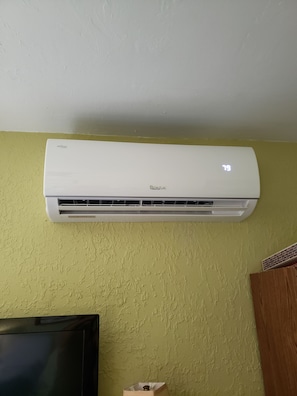 A white air conditioner mounted on a textured yellow wall.