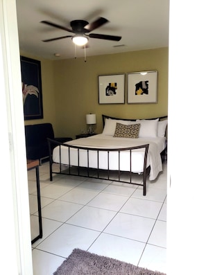 A bedroom with a bed, a ceiling fan, a nightstand, a lamp, and two framed pictures on the wall.