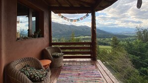 A wooden deck with wicker chairs and a colorful rug, overlooking a mountainous landscape.