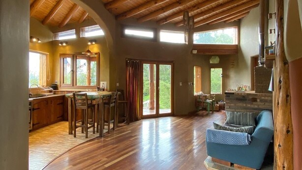 A spacious living area with a wooden ceiling, a kitchen with a bar, and a seating area with a sofa and chairs.