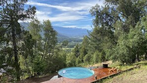 A hot tub on a wooden deck with a view of mountains and trees.
