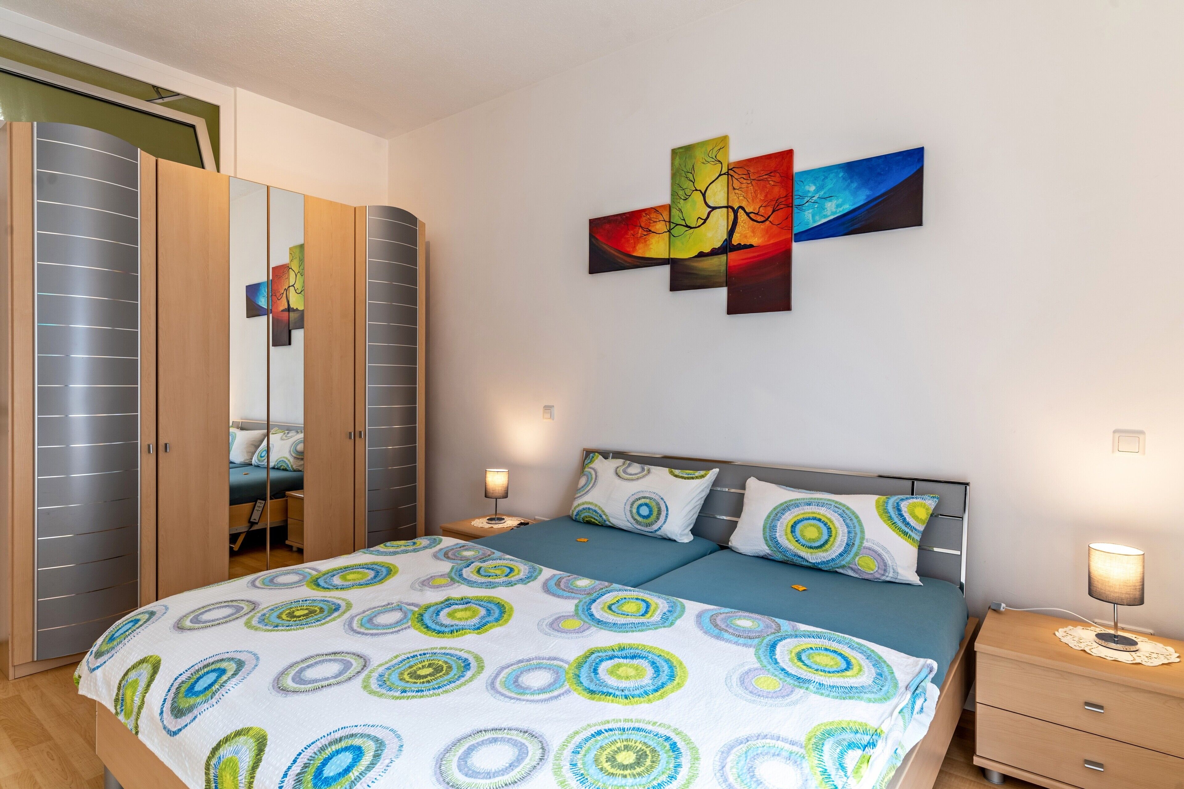 A bedroom with a bed, nightstands, a wardrobe, and a wall with a painting.