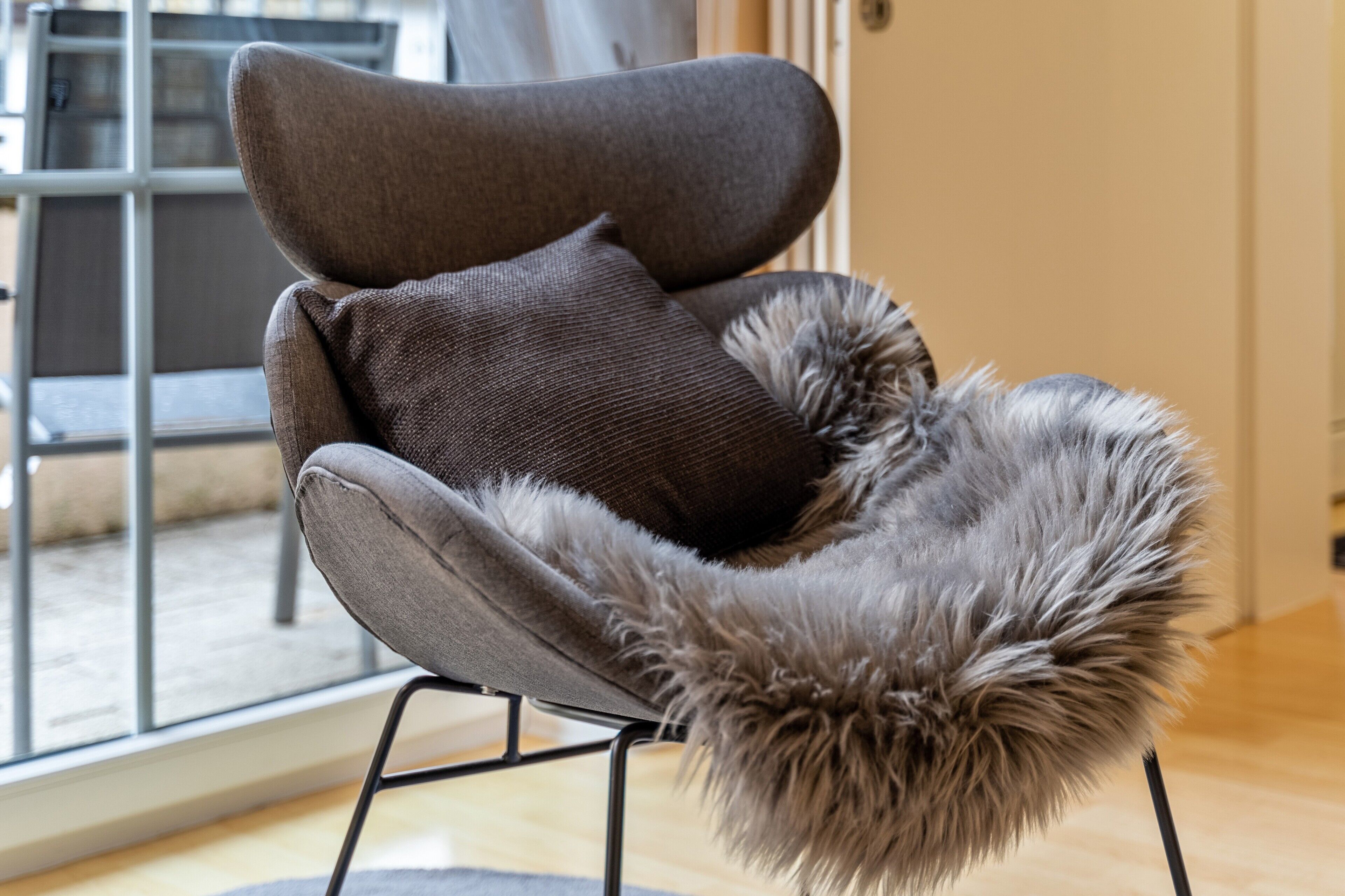 Una silla moderna con un plaid de piel y un cojín.