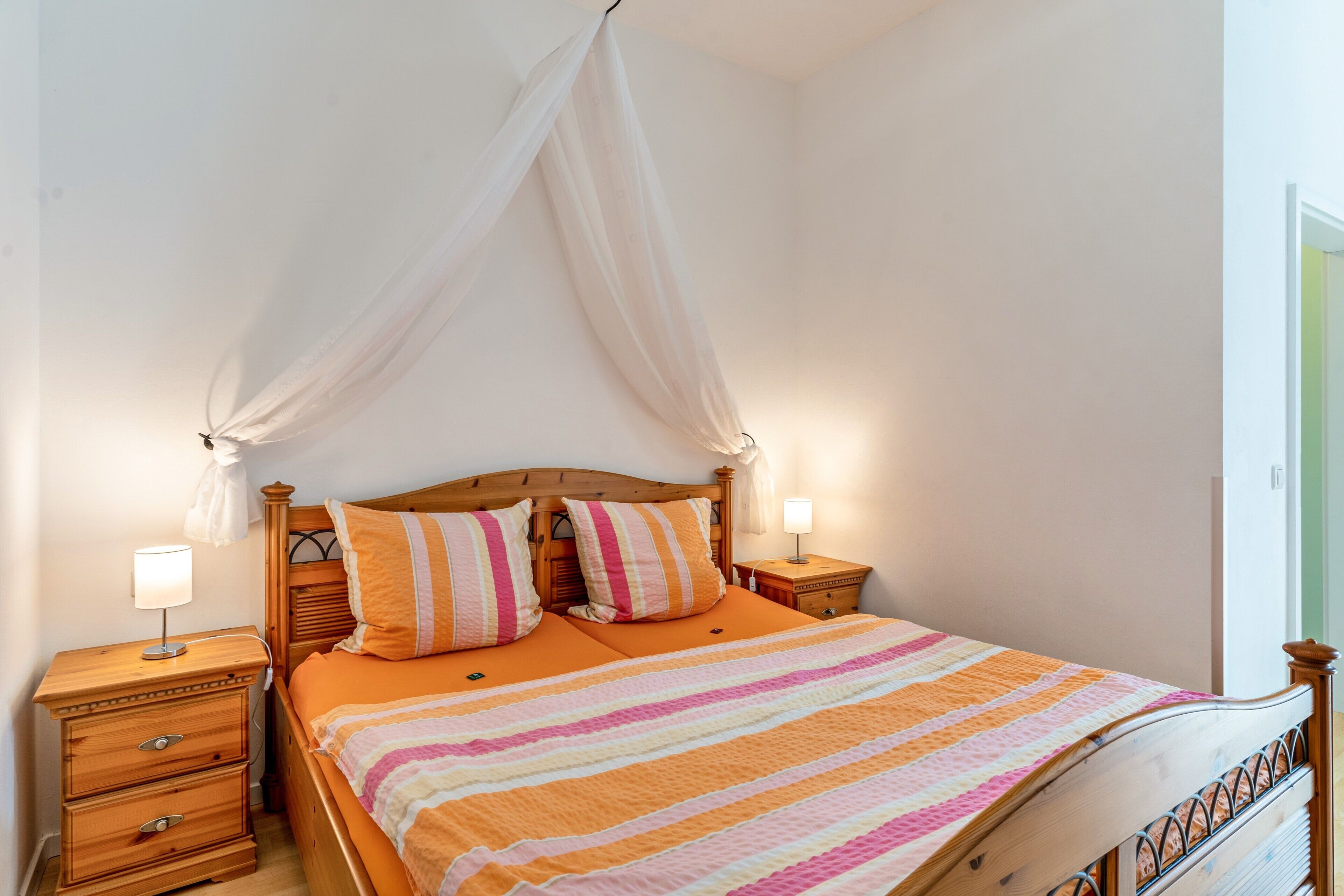 A bedroom with a wooden bed, two bedside tables, a canopy, and a striped bedspread.