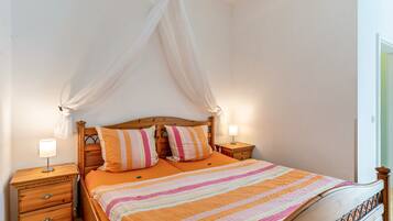 A bedroom with a wooden bed, two bedside tables, a canopy, and a striped bedspread.