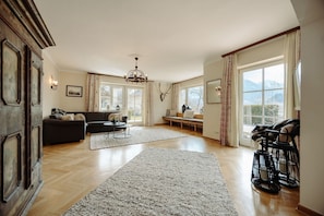 Ein geräumiges Wohnzimmer mit großem Fenster, einer Chandelieber, einer Couch und einem Kamin.