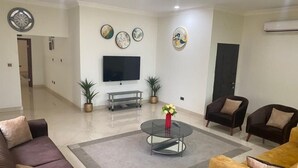 A living room with a flat-screen TV, two potted plants, a round coffee table, and a sofa.