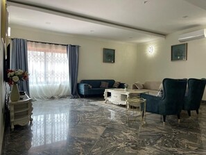A spacious living room with a marble floor, a blue sofa, a white coffee table, and a dark armchair.