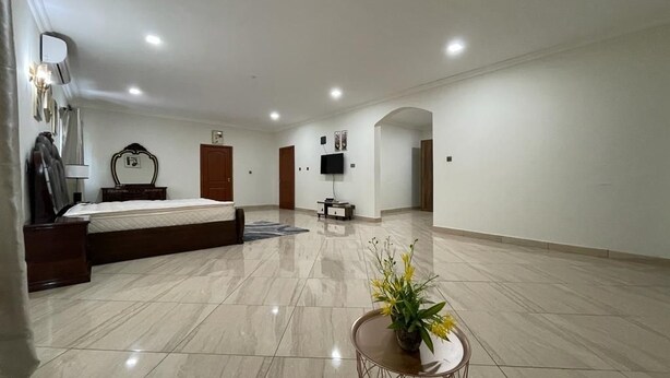 A spacious hotel room with a large bed, a small round table with a vase of flowers, a flat-screen TV, and a mirror on the wall.