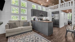 A modern kitchen with grey cabinets, a central island, and a dining area with a chair. - Menlo GA Tiny Home Experience! Beautiful Drive (Menlo)