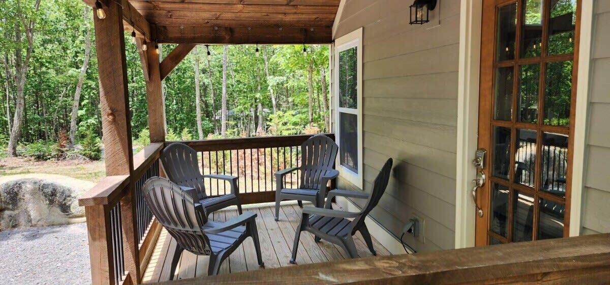 Eine Holzterrasse mit drei Adirondack-Stühlen, einem Hollerleger und einer Tür mit Glasfeldern.
