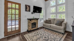 A living room with a stone fireplace, a beige sofa, a patterned rug, and a TV mounted on the wall. - Menlo GA Tiny Home Experience! Beautiful Drive (Menlo)