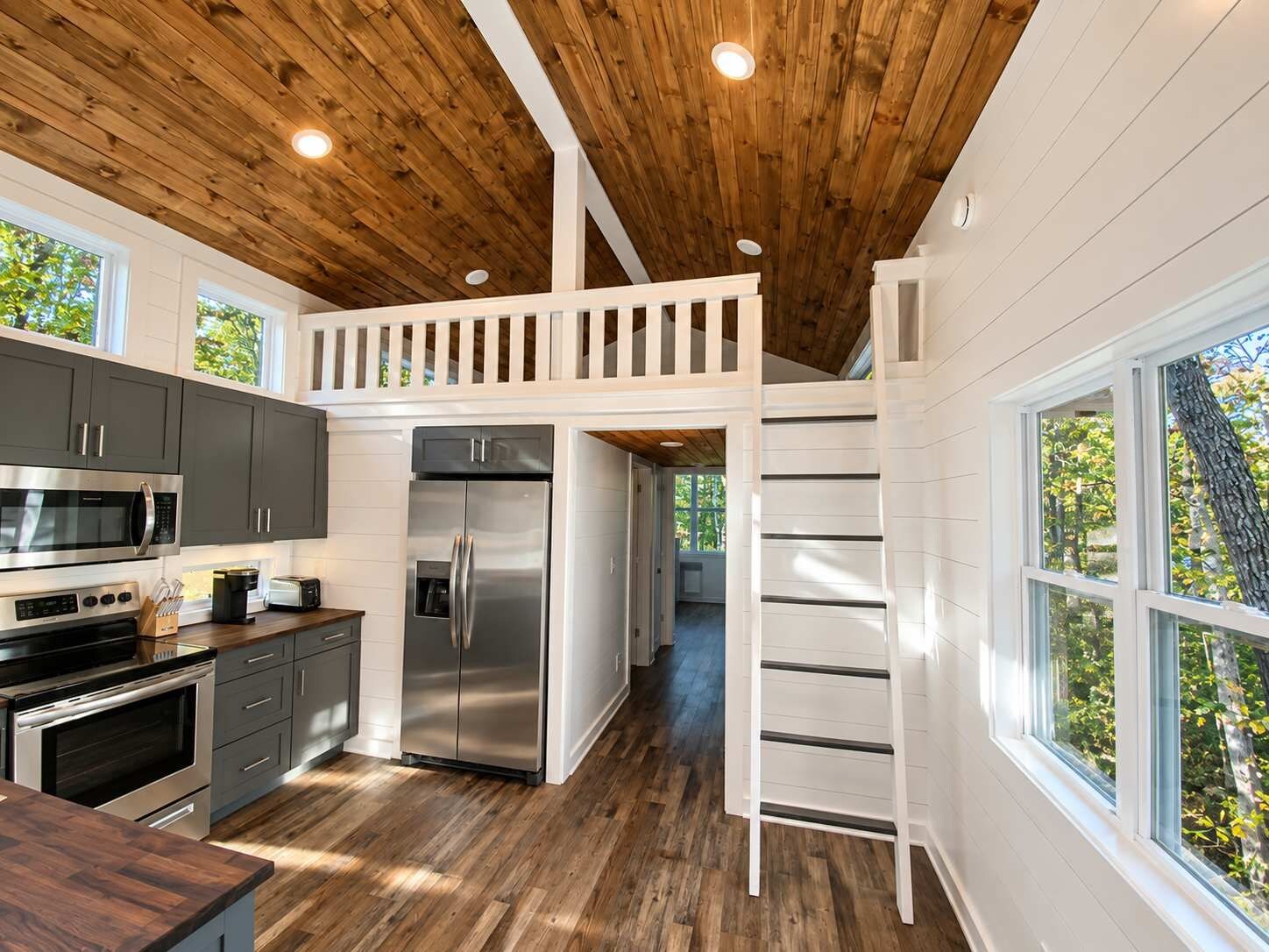 Eine moderne Küche mit Holzboden, Edelstahlgeräten und Blick ins Freie durch große Fenster.