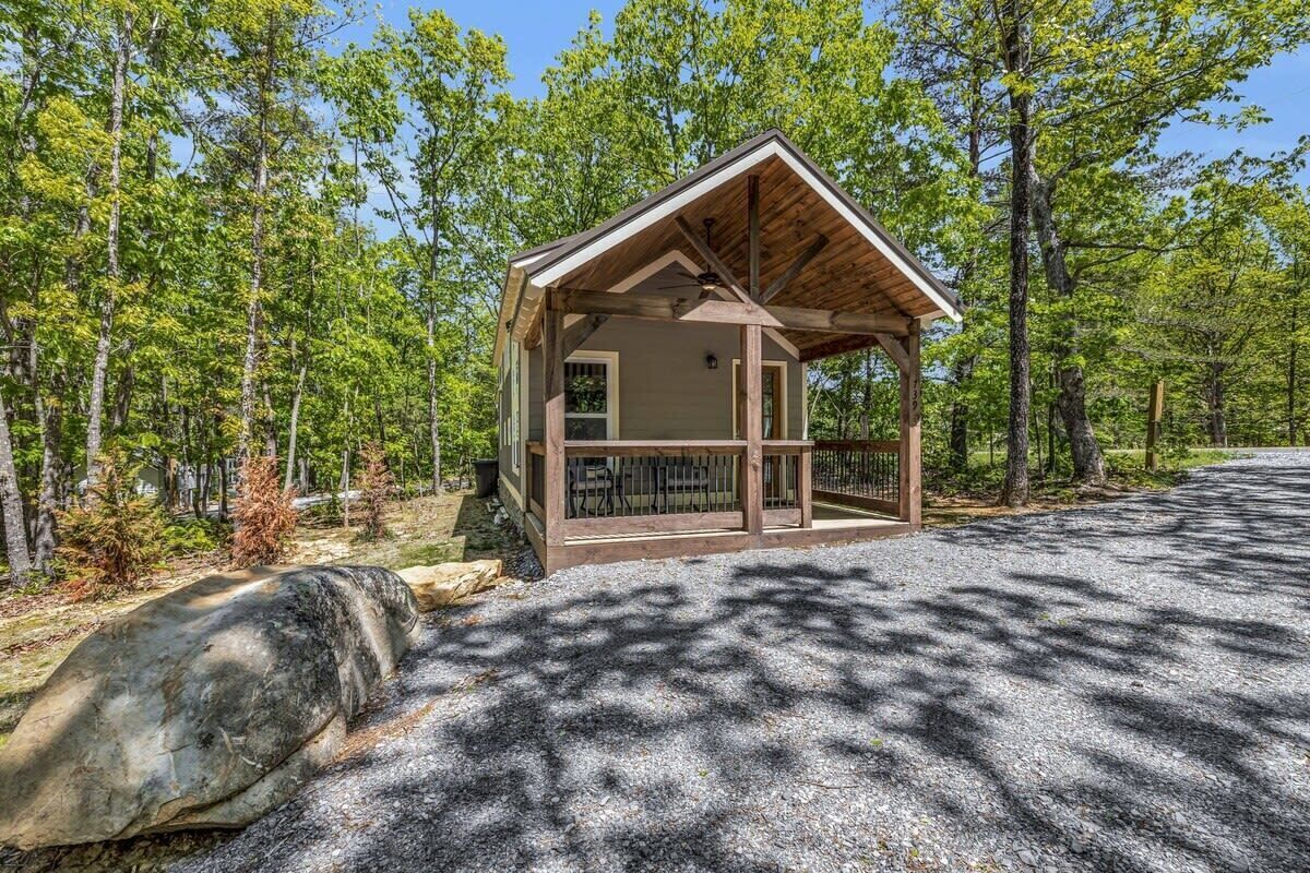 Une petite cabane en bois, dotée d’une véranda et entourée d’arbres.