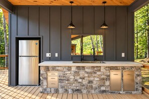 A modern kitchen with a stone island, stainless steel refrigerator, and pendant lighting. - Wild Indigo Haus | Pickleball · Sauna · Pool (Menlo)