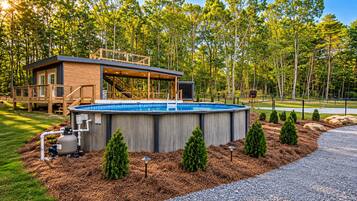 Una casa moderna con terraza de madera, piscina y jardín bien cuidado con árboles y arbustos.