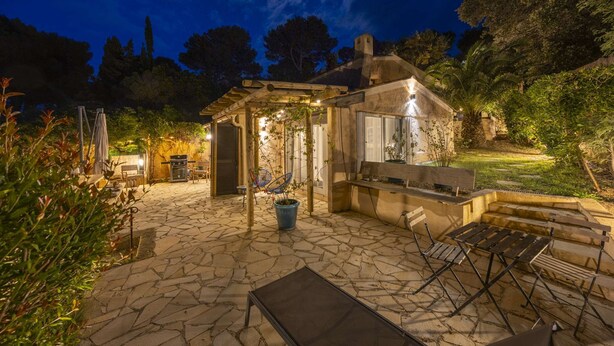A stone patio with outdoor furniture, a pergola, and a small garden area at night. - Cavalaire sur mer Mas Boubanette (CAVALAIRE SUR MER)