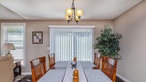 Comedor con una mesa de madera, sillas, una araña, una planta y una ventana con persianas.