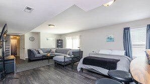 Una habitación moderna y bien iluminada con un sofá gris, una cama, una mesita y un escritorio con una silla.